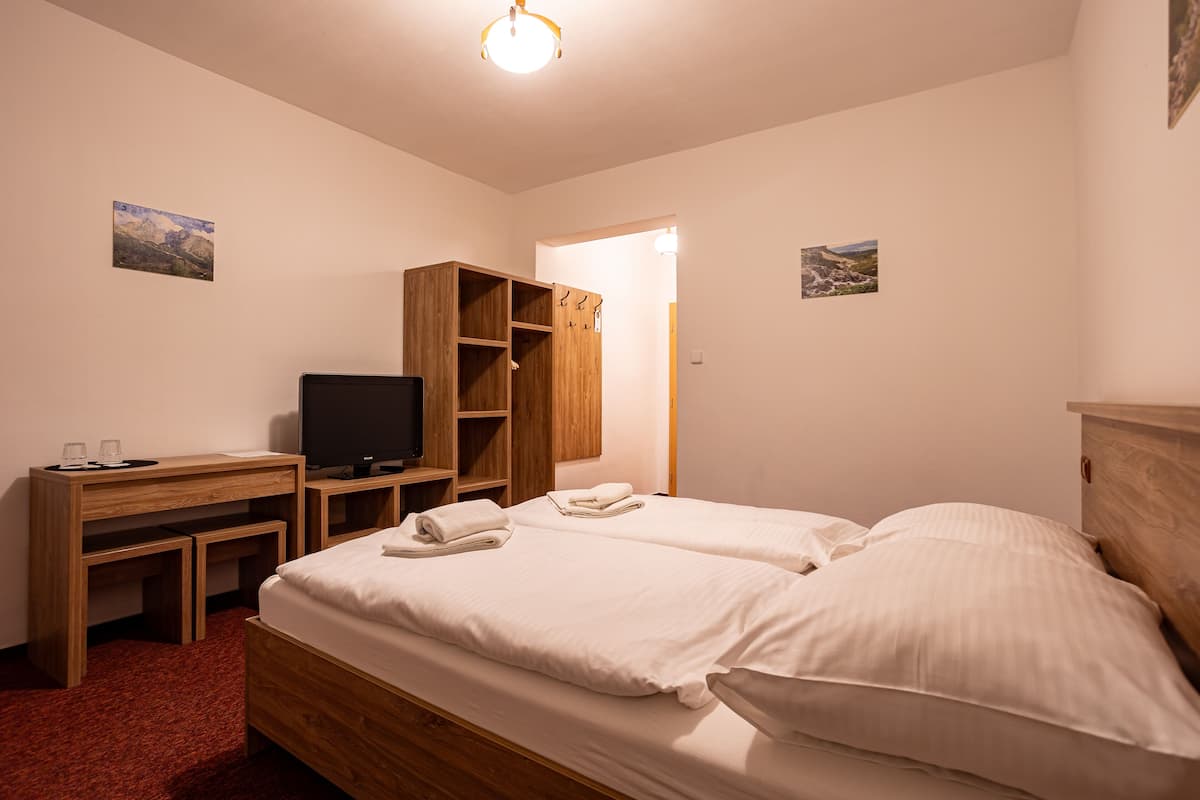 A hotel room with a bed, a desk with a TV, wooden wardrobe, and two wall-mounted pictures.