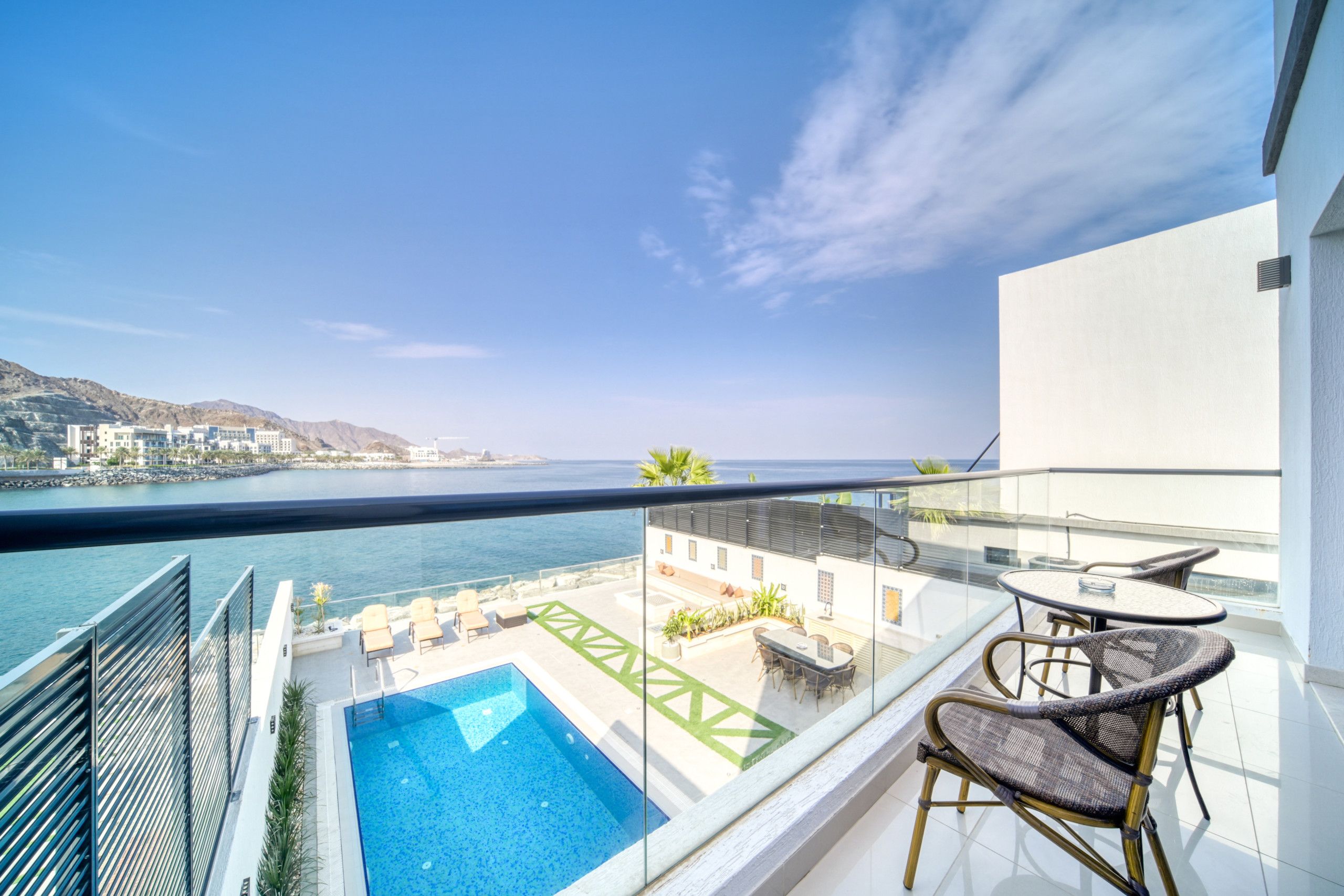 A balcony with a pool, outdoor seating, and a view of the sea and cityscape.