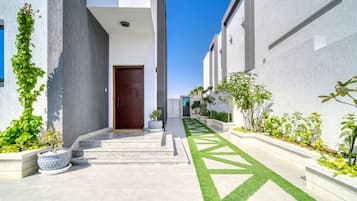 A modern building with a central entrance, a paved pathway, and a variety of plants.