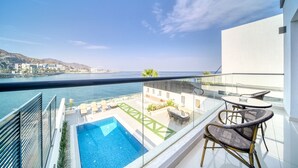 A balcony with a pool, outdoor furniture, and a view of the sea and hills.