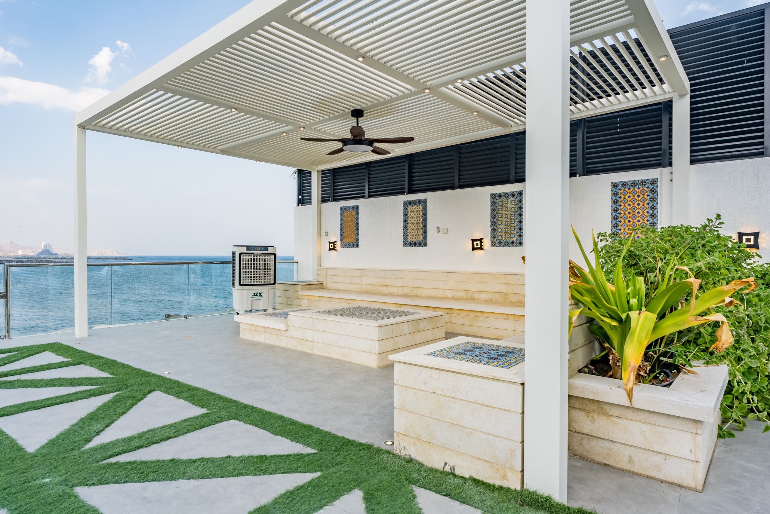 A covered outdoor area with a ceiling fan, a view of the sea, and a seating area with planters.