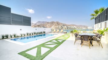 A rooftop pool area with a clear view of a mountain range and a body of water in the distance.