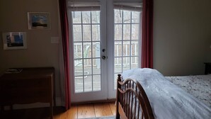 A bedroom with a wooden bed, a nightstand, a desk, and a large window with curtains.