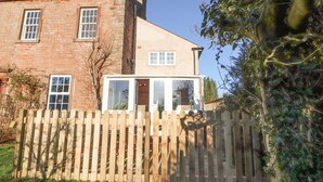 A two-story house with a brick facade and a wooden fence in front. - Hillside Hideaway (Wigton)