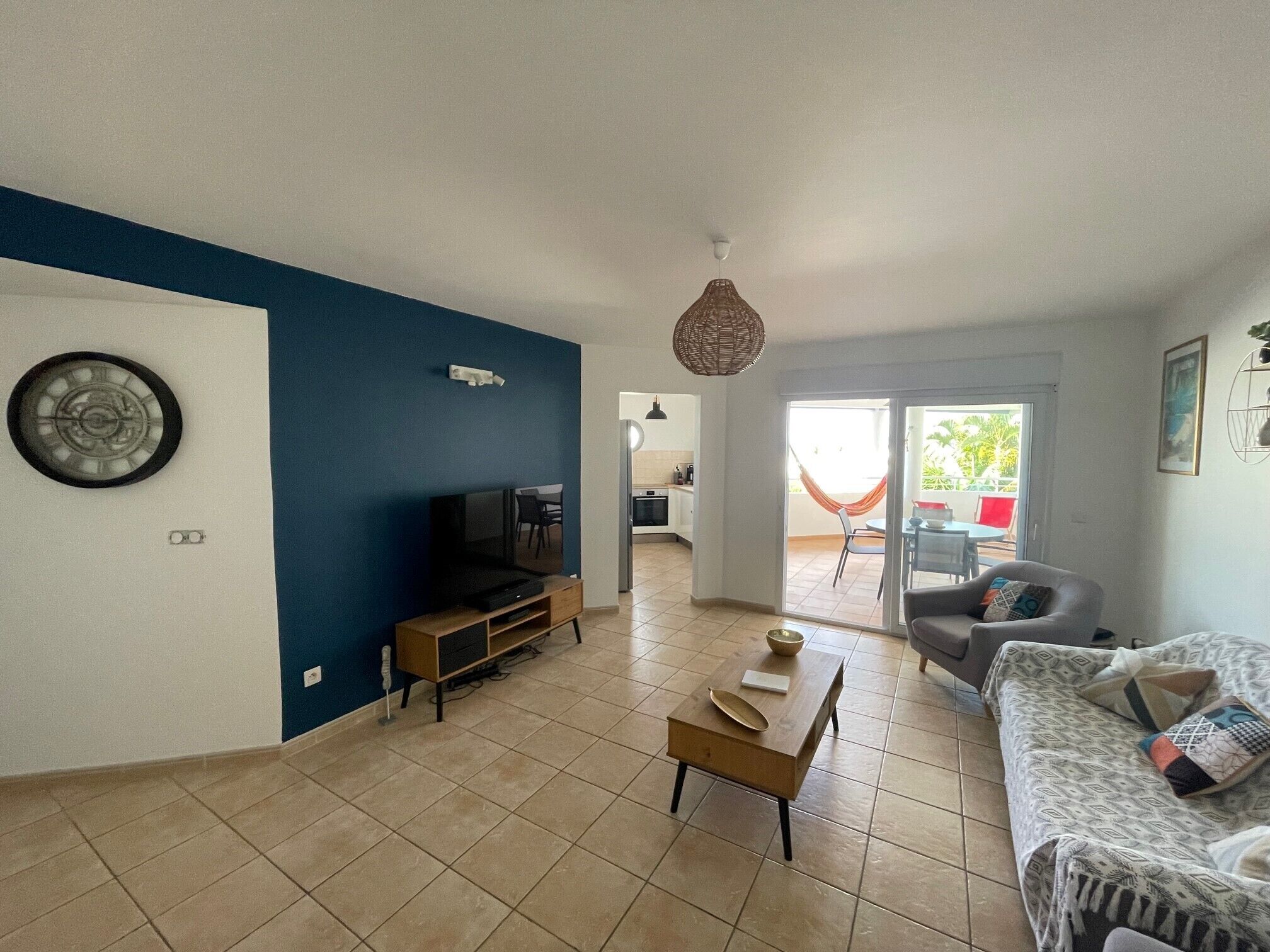 A living room with a TV, a coffee table, and a sofa. There is a kitchen in the background.