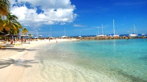 Una playa con agua turquesa cristalina, arena blanca y varios veleros anclados cerca de la orilla.