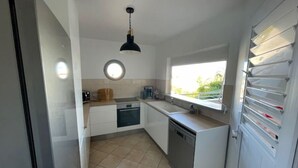 Cocina compacta con alacenas blancas, lavavajillas, pileta y ventana que proporciona luz natural.