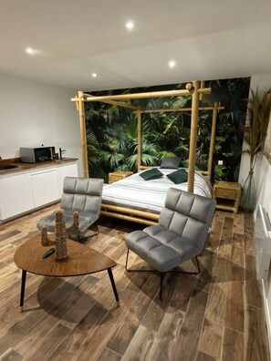 A bedroom with a bed, two armchairs, a coffee table, a nightstand, and a wall mural. - Jungle Room Avec Baignoire Balnéothérapie ! (Sotteville-lès-Rouen)