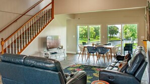 A spacious living area with a staircase, a dining table with chairs, a sofa, and a TV. - Waterfront with Boat Slip, Sports Bar, SUP'S, Great Location! (Willis)