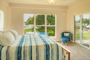 A bedroom with a large window, a bed with a striped bedspread, a chair, and a view of a backyard.