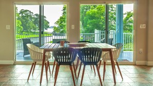 A dining area with a table and chairs, large sliding glass doors leading to an outdoor patio with a view of a lake and trees. - Waterfront with Boat Slip, Sports Bar, SUP'S, Great Location! (Willis)