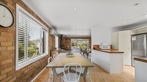 Una cocina con una mesa de madera, sillas blancas, un reloj en la pared y vistas al exterior.