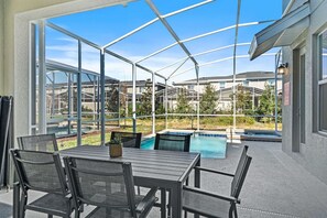 An outdoor patio with a pool, covered seating area, and a view of neighboring houses.