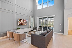 A spacious living area with a gray sofa, a coffee table, and a TV mounted on the wall. - 5BR Home w/ Game & Themed Rooms at Champions Gate (Kissimmee)