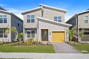 A modern two-story residential building with a stone facade, a yellow garage door, and a well-maintained lawn with small trees.
