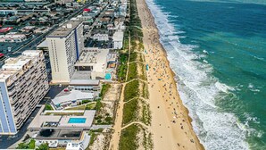 Vista aérea de una ciudad costera con una extensa playa de arena, un edificio de gran altura y un complejo de piscinas.