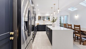 A modern kitchen with a central island, black cabinetry, stainless steel appliances, and pendant lighting.