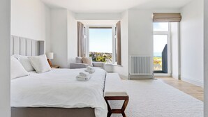 A modern bedroom with a large bed, bedside tables, a bench, a window with curtains, and a radiator.