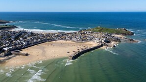 An aerial view of a coastal town with a beach, a fortified wall, and buildings along the shore.