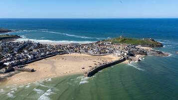 An aerial view of a coastal town with a beach, a fortified wall, and buildings along the shore.