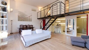 Un salón amplio con una cama grande, una escalera, una zona de comedor y una cocina visible a través de una puerta abierta.