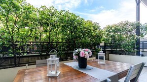 Una mesa de madera con dos faroles blancos y un florero con flores, ubicada al aire libre con vista a exuberante follaje.