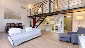 Amplia sala de estar con un sofá, una mesa de comedor y una escalera que sube a un nivel superior.