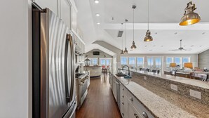 A spacious kitchen with a large island, stainless steel appliances, and pendant lighting. - Crew Quarters -- 16BR Oceanfront with Elevator, Pool and More! (Corolla)