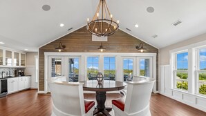 A spacious dining area with a large round table, white chairs, and a wooden ceiling. - Crew Quarters -- 16BR Oceanfront with Elevator, Pool and More! (Corolla)
