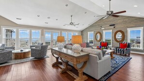 A spacious living room with a high ceiling, large windows, and a view of the ocean. - Crew Quarters -- 16BR Oceanfront with Elevator, Pool and More! (Corolla)