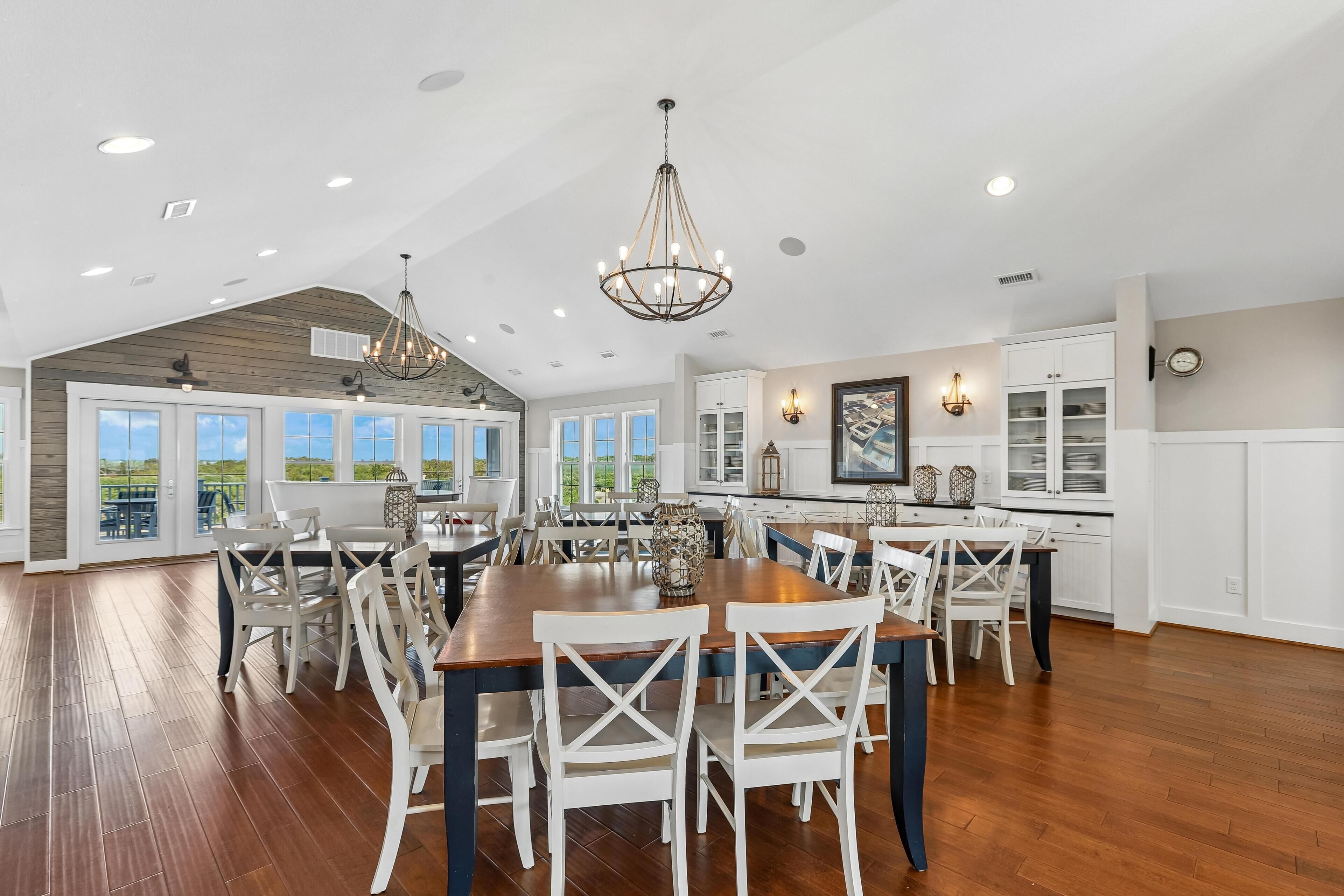 A spacious dining area with a large wooden table, white chairs, and a chandelier.