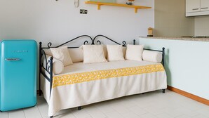 A room with a bed, a turquoise refrigerator, a kitchen area, and a shelf with a bowl. - VivimiHome–Mare e relax nel cuore di Porto Rotondo (olbia)