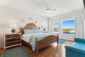 A bedroom with a wooden bed, a nightstand, a chair, and a view of the outdoors. - Knot Home -- 16BR OF in Corolla with Pool, Elevator, Theater, Game Room and More! (Corolla)