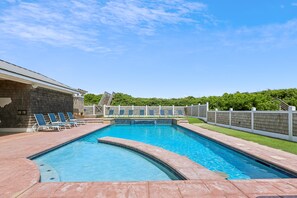 A rectangular swimming pool with a tiled edge, surrounded by a brick deck. There are lounge chairs along the pool's edge and a white fence with a gate. - Knot Home -- 16BR OF in Corolla with Pool, Elevator, Theater, Game Room and More! (Corolla)