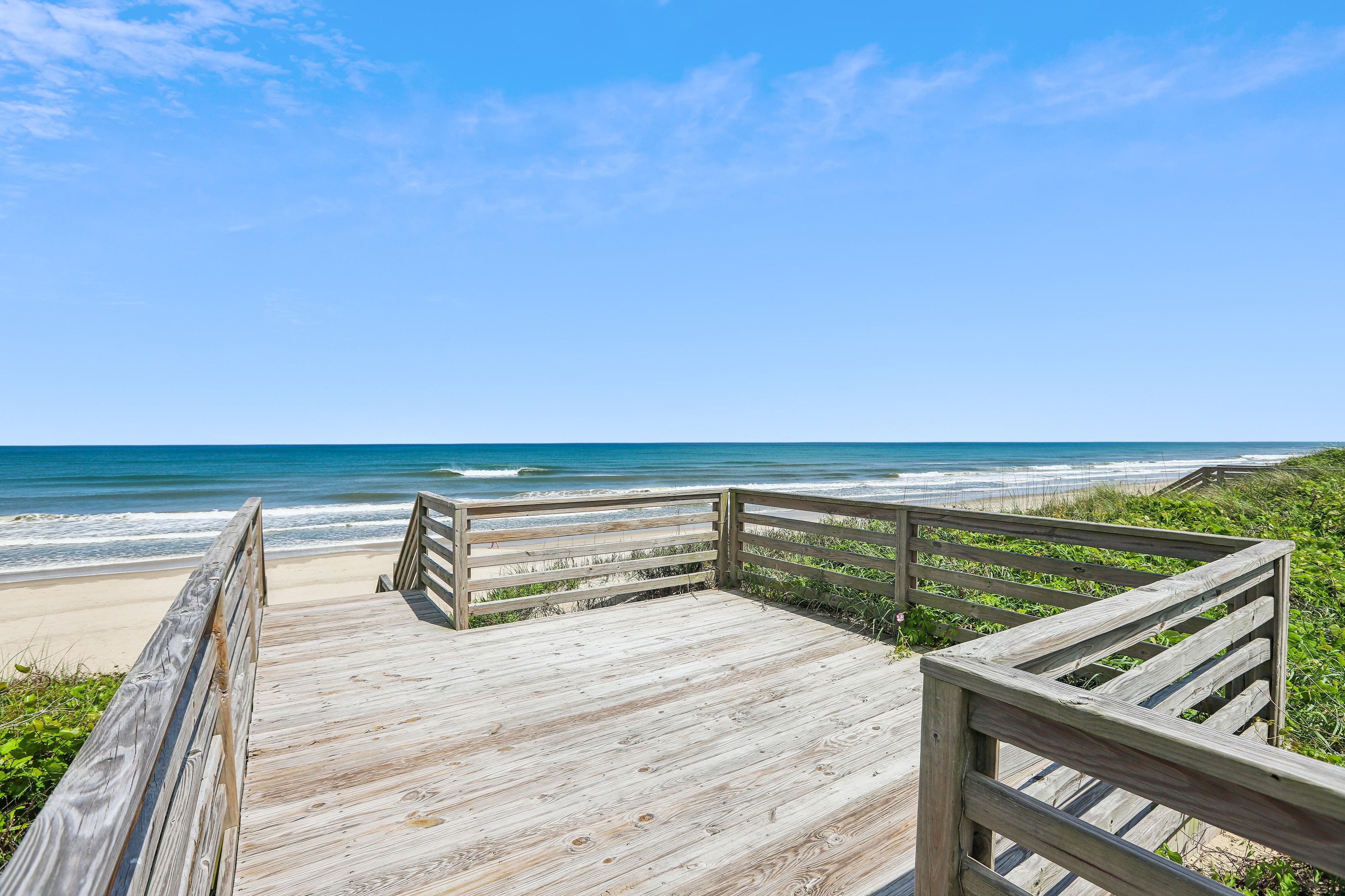 A wooden boardwalk leading to a beach with ocean views.