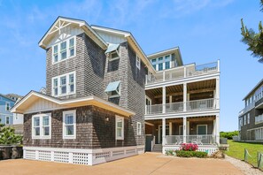 A two-story building with a balcony on the second floor. - Knot Home -- 16BR OF in Corolla with Pool, Elevator, Theater, Game Room and More! (Corolla)