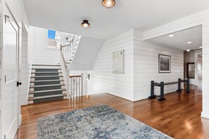 Un ampio corridoio con pavimento in legno, una scala con tappeto decorato e un punto luce a parete.