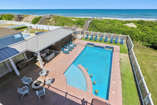 A pool area with lounge chairs, a barbecue, and a view of the ocean. - Knot Home -- 16BR OF in Corolla with Pool, Elevator, Theater, Game Room and More! (Corolla)