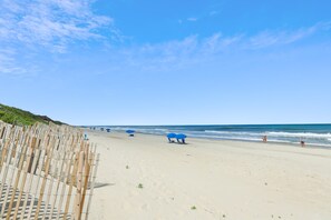 A beach with a wooden fence, blue umbrellas, and a clear sky. - Knot Home -- 16BR OF in Corolla with Pool, Elevator, Theater, Game Room and More! (Corolla)