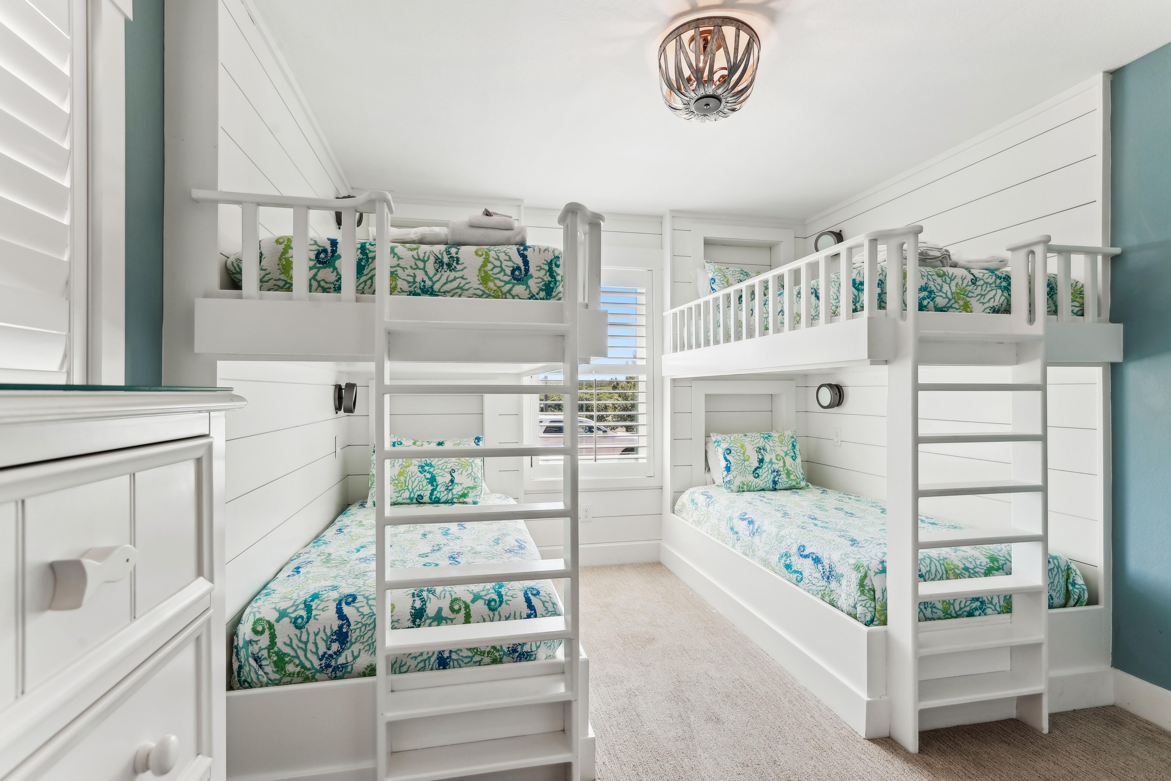 A children's bunk bed room with white railings and a decorative ceiling light.