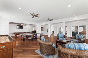 A spacious living room with a pool table, wicker furniture, and ceiling fans.