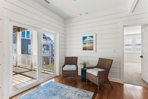 A room with a large sliding glass door leading to a balcony, wicker chairs, a blue rug, and a framed picture on the wall.