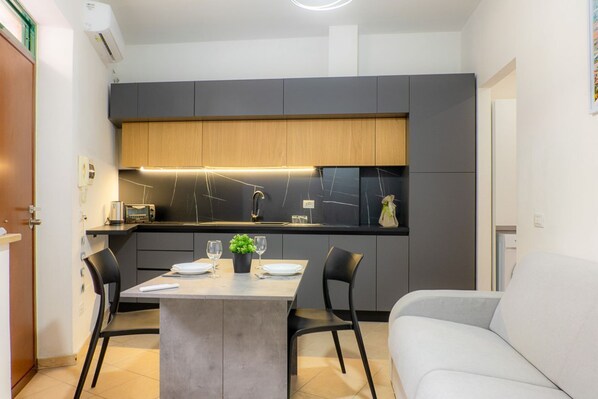 A compact kitchen with a central island, dark cabinetry, and a modern light fixture.