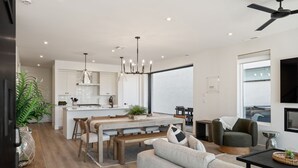 A modern kitchen with white cabinets, a dining area with a bench, and a living room with a sofa and a TV. - The Beach Club: Desert Color Lagoon + Beaches (St. George)