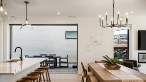 A modern kitchen with a central island, bar stools, and a dining area with a wooden table and chairs. - The Beach Club: Desert Color Lagoon + Beaches (St. George)