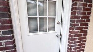 A white door with a window, a metal door handle, and a brick wall.