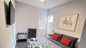 A bedroom with a bed, a ceiling fan, a TV mounted on the wall, and a painting above the bed.