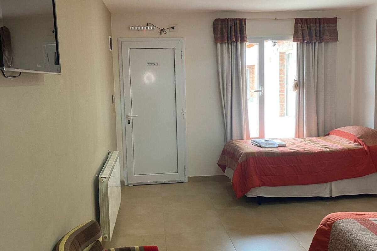 A hotel room with two beds, a chair, a TV mounted on the wall, and a door.