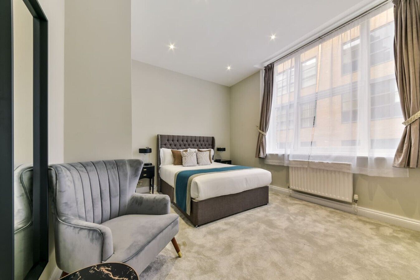 A hotel room with a bed, a chair, a bedside table, and a window with curtains.