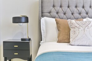 Un lit bien fait, avec une tête de lit capitonnée, une lampe de chevet et une petite table de chevet dotée de tiroirs.